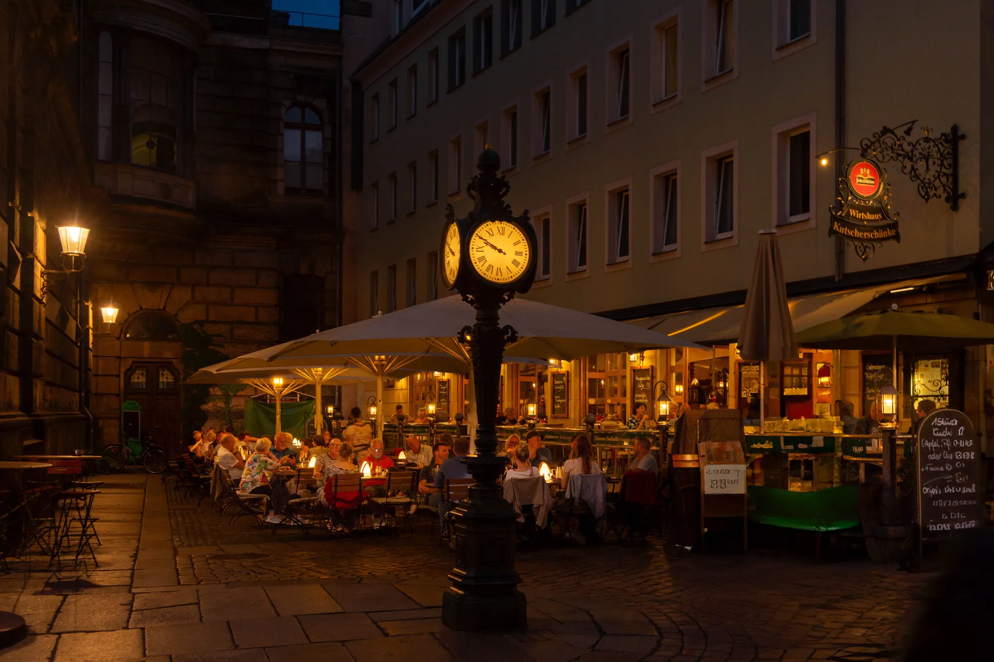 An old-town street lined with cafés and lit storefronts in the evening